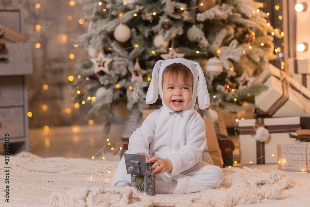Merry Christmas and Happy New Year. Little happy girl dressed as a white bunny plays with a lantern on the background of a beautifully decorated Christmas tree.