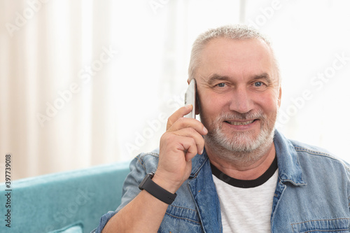 Portrait of adult gray-haired man who smiles at camera and talks on cell phone