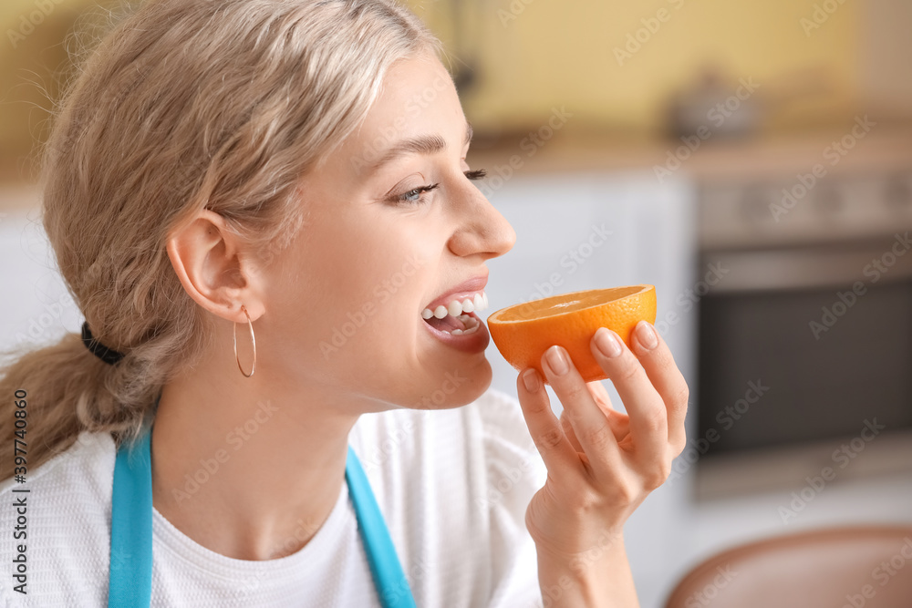 Beautiful young woman eating fresh orange in kitchen Beautiful young woman eating fresh orange in kitchen