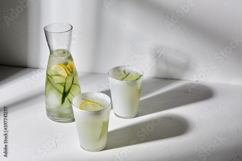 drink, detox and diet concept - glasses with fruit water or lemonade with lemon and cucumber dropping shadows on white surface