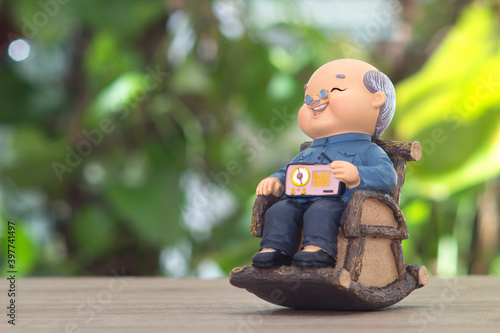 In front of the blurred green plant background, a sculpture of an old grandfather sitting in a rocking chair happily enjoying the retirement life photo