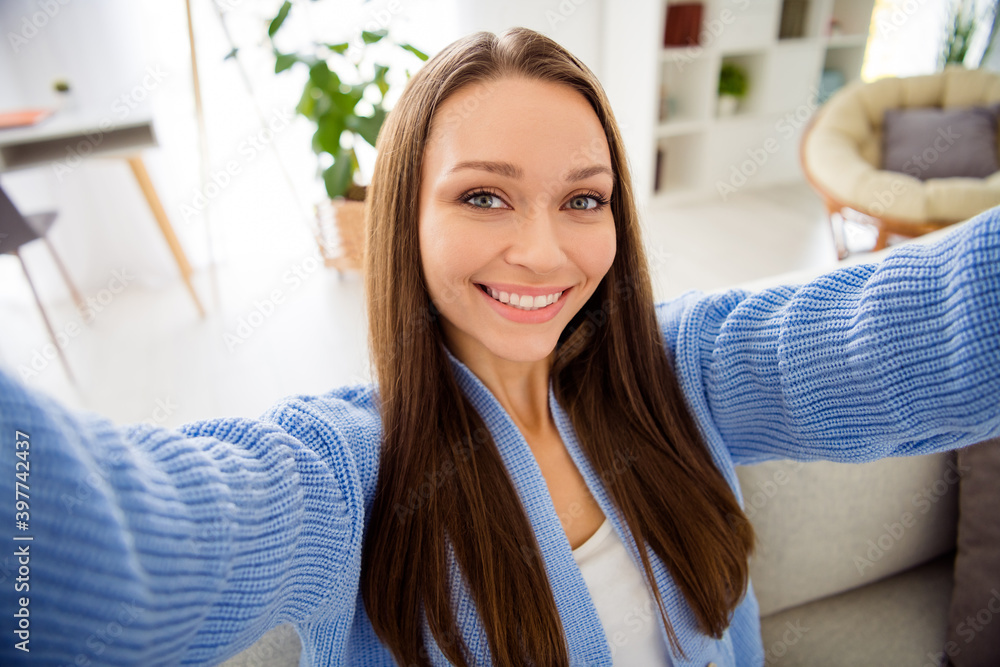 Self-portrait of charming cheerful girl sitting on divan spending free spare time in light flat house apartment living-room indoor