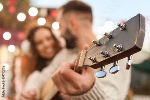 Young man playing guitar for his girlfriend on Christmas eve
