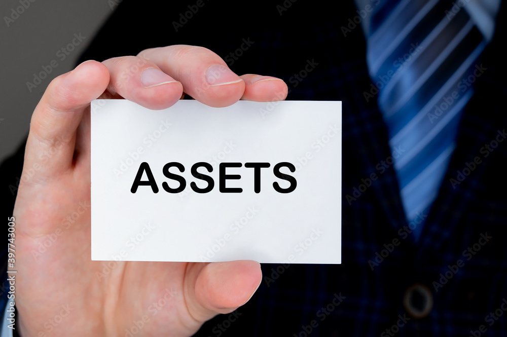 Close-up of man's hand holding and showing visiting card with ASSETS word on it. Close-up of man's hand holding and showing visiting card with ASSETS word on it.