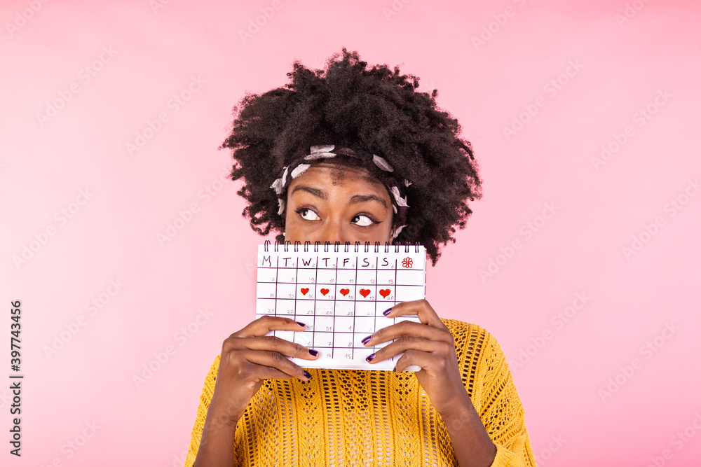 Portrait of a funny young African American girl in hiding behind a  menstrual periods calendar and looking away at copy space isolated over  pink background. Female Period calendar Stock Photo | Adobe