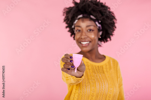 Serious dark skinned woman holds bell shaped menstruation cup for inserting in vagina, trapping menstrual fluid and leakage protection, tells secret information and tips how to use it, makes hush sign