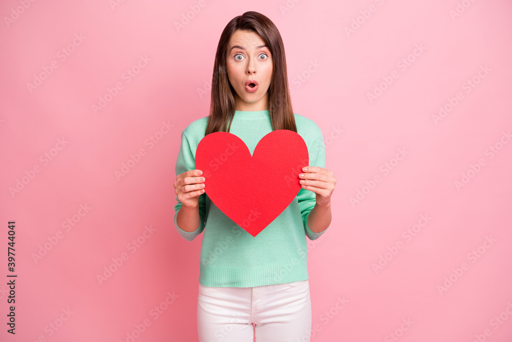 Portrait of attractive astonished girl holding in hands red heart pout lips isolated over pink pastel color background Portrait of attractive astonished girl holding in hands red heart pout lips isolated over pink pastel color background