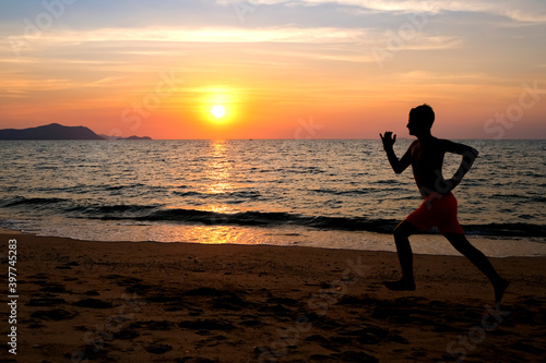 Silhouette of a young man running at the beach at sunrise with the sun in the background. Staying fit and healthy banner