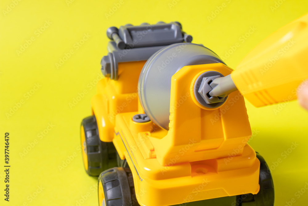 Fototapeta premium The toy typewriter is a concrete mixer and screwdriver that twists the cog on a yellow background. Photos for a toy store and educational activities. Early development of children.