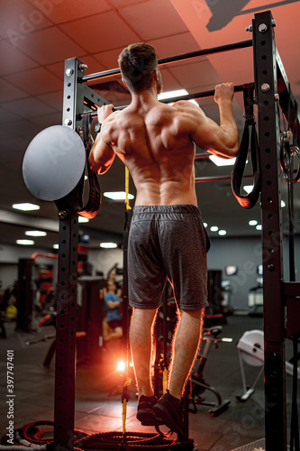 A portrait of a hot handsome strong guy man without a shirt against gym background on the horizontal bar. Male beauty concept. View from the back. Closeup.