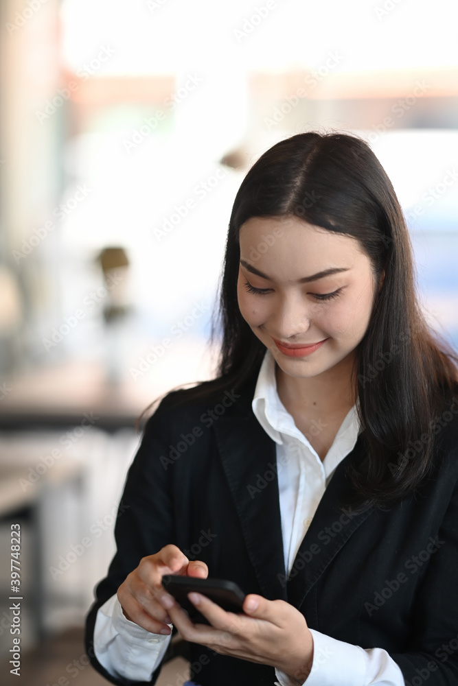 Portrait of a smiling businesswoman in black suit using mobile phone in office.