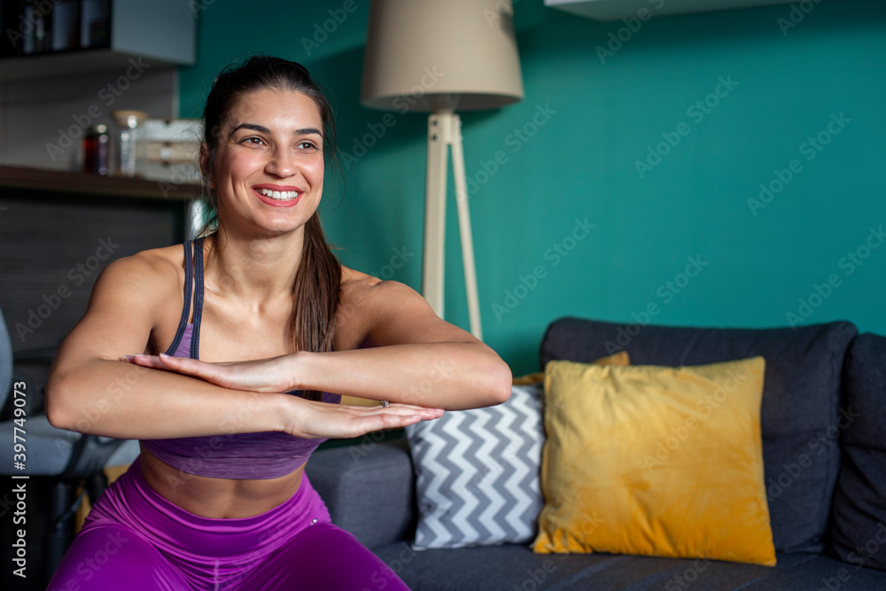 A smiling fit woman is training and doing squats at home.