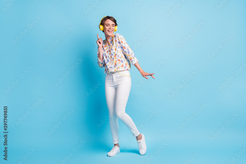 Full body photo of attractive charming young lady closed eyes dance listen song headset isolated on blue color background Full body photo of attractive charming young lady closed eyes dance listen song headset isolated on blue color background