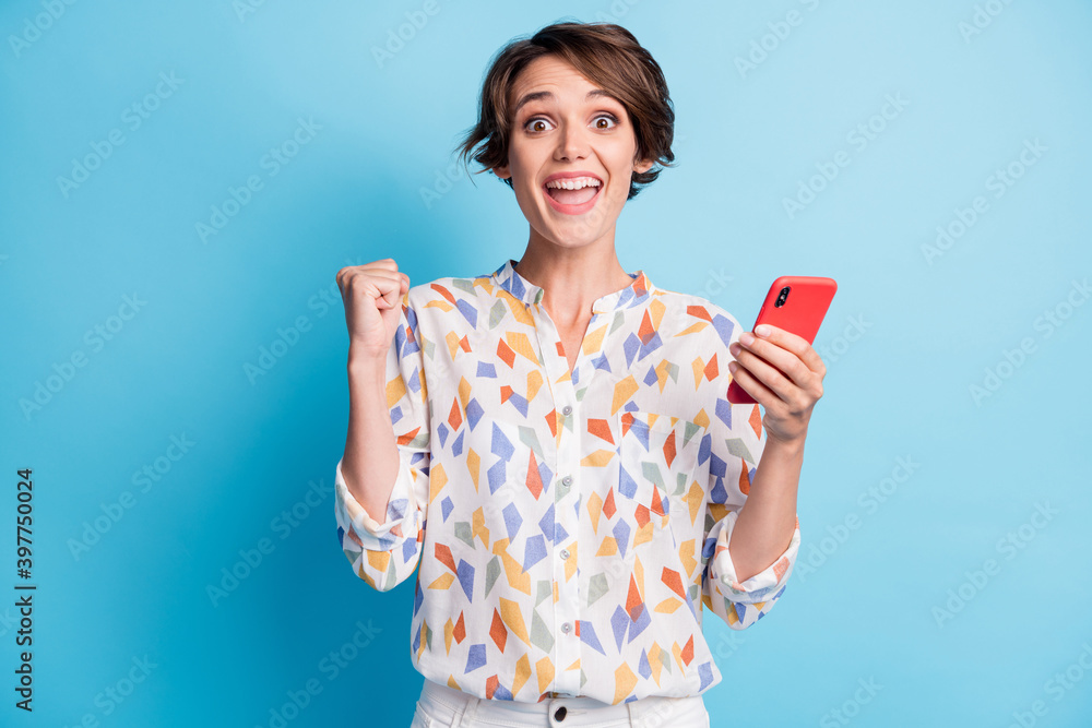Photo of victorious brown bob haired girl raise fists hold phone amazed isolated on blue color background Photo of victorious brown bob haired girl raise fists hold phone amazed isolated on blue color background