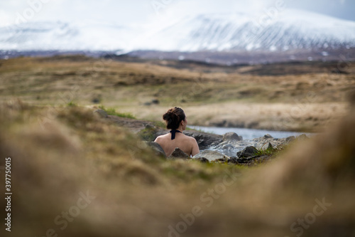 A woman in a hot spring in Iceland looking at snowy mountains in the distance