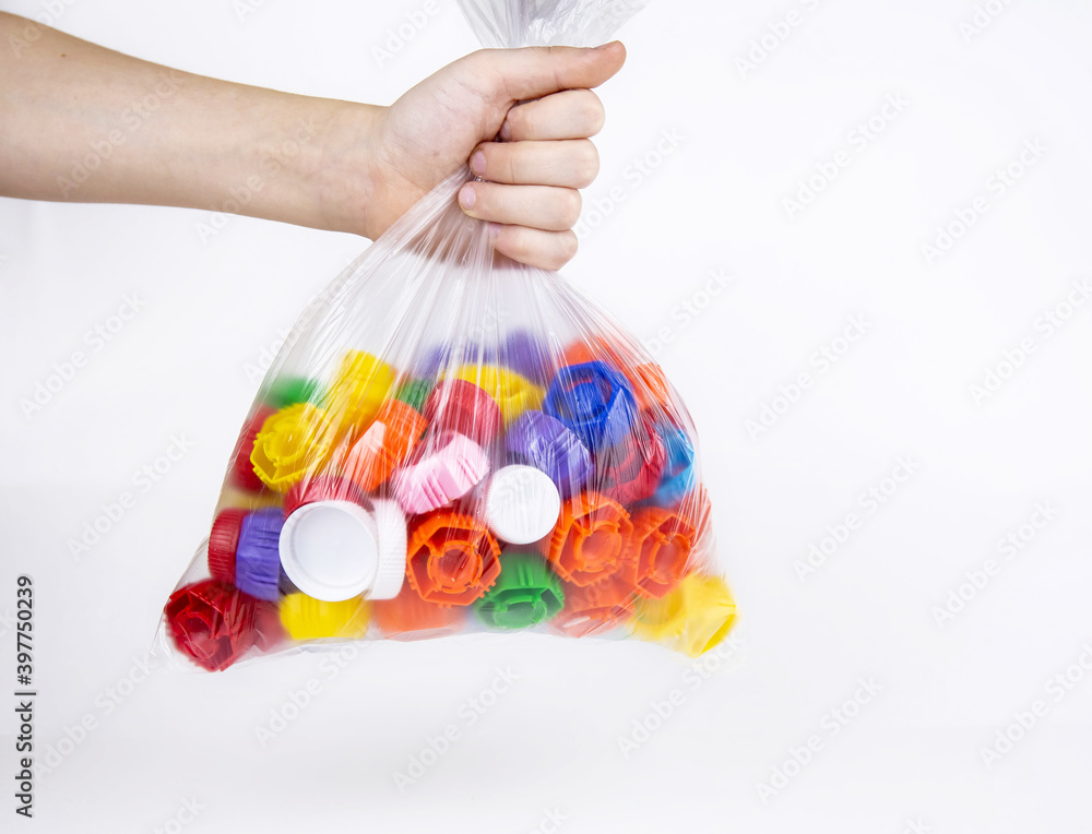 Child's hand holds a package with plastic bottle caps on a white background. Ecology and recycling concept.