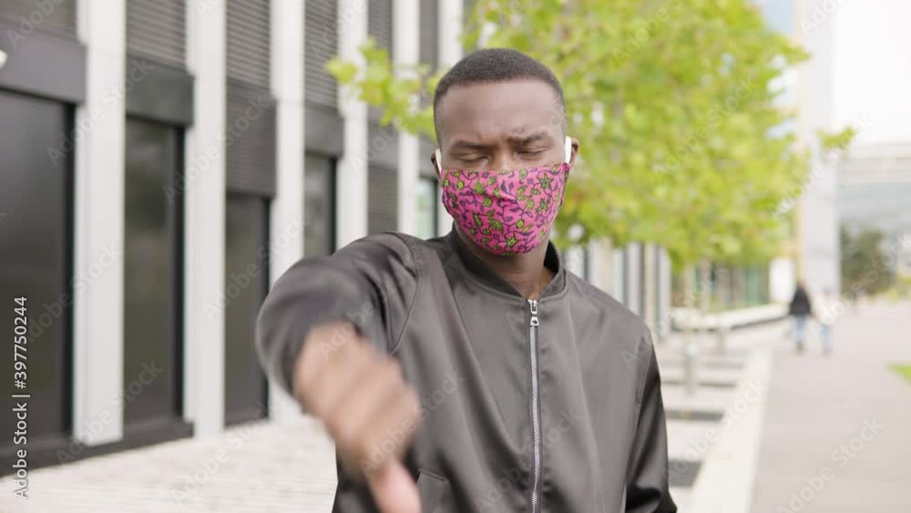 A young black man in a face mask shows a thumb down to the camera and ...