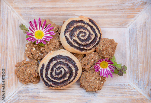 selbstgebackene Vollkorn Haferflockenplätzchen und Mohnschnecken auf einem Holztablett, 2 Asternblüten photo