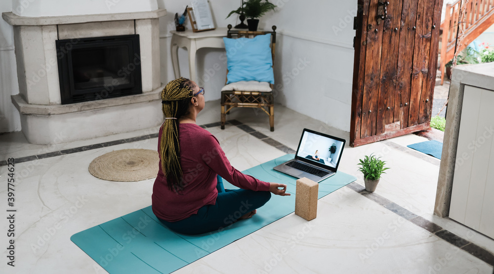 African senior woman doing online yoga lesson at home during coronavirus outbreak - Old female person meditating using computer laptop - Technology and zen concept - Focus on hand - obrazy, fototapety, plakaty 