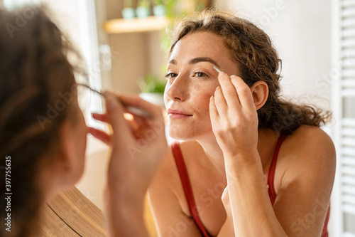 Young woman plucking eyebrows with tweezers