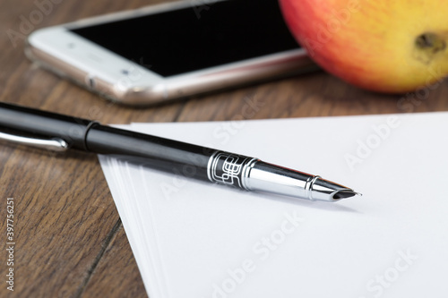 fountain ink pen with cap on table with sheets of white paper and phone with red apple