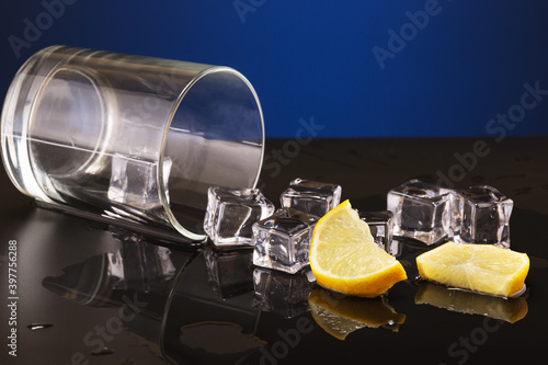 overturned glass transparent glass with spilled liquid and lemon wedges with ice cubes