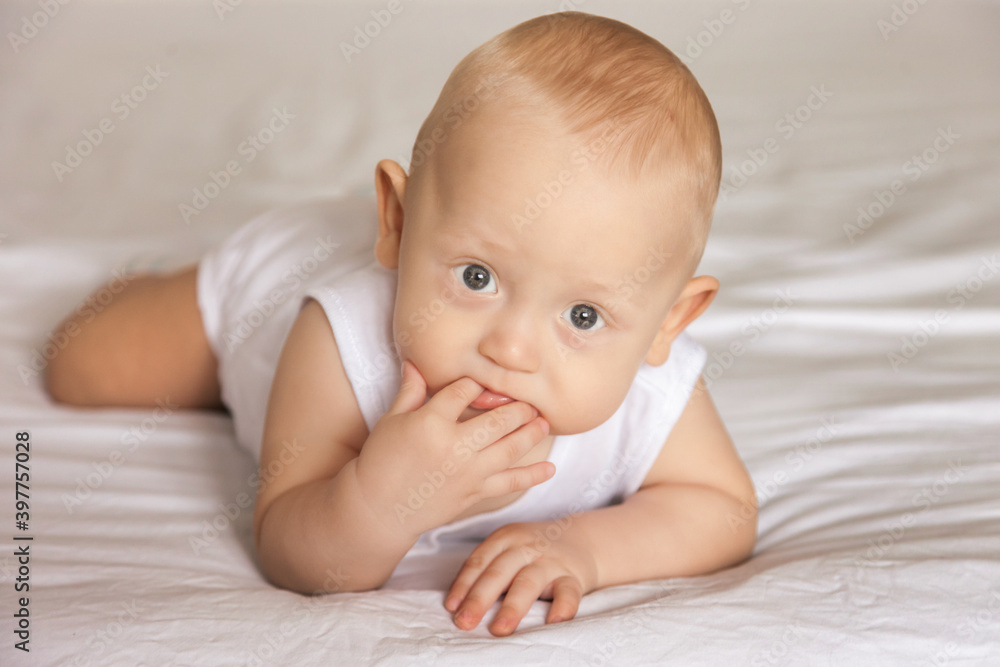 A charming boy licks his fingers while lying on his stomach. The view of a serious person