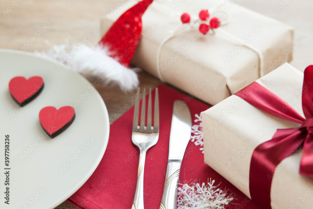 Festive table setting for Valentine's Day with plate, gift boxes, fork, knife and hearts on a wooden table. Festive table setting for Valentine's Day with plate, gift boxes, fork, knife and hearts on a wooden table.