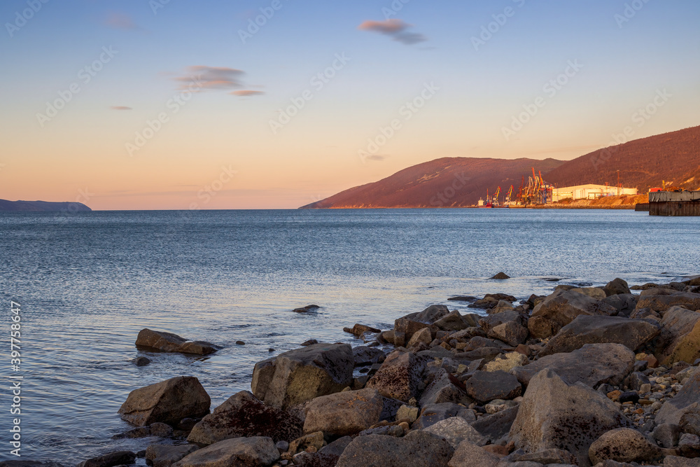Morning seascape. View from the coast to the sea bay, mountains and cargo seaport. Beautiful landscape of the Nagaev Bay of the Sea of ​​Okhotsk. Sea port of the city of Magadan, Russian Far East.
