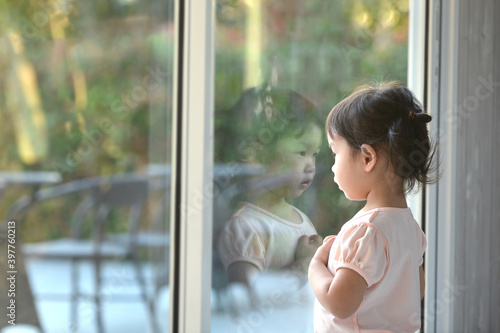 Sad asian little girl looking outside through the window