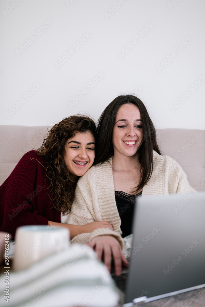 two white women looking at the laptop on the bed while smiling two white women looking at the laptop on the bed while smiling