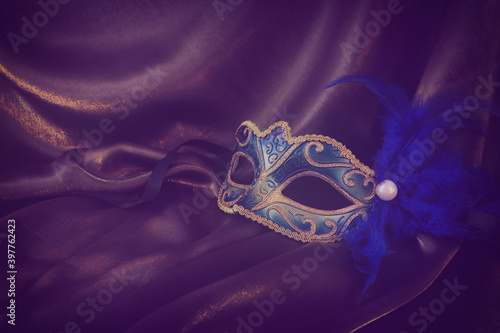 Photo of elegant and delicate gold Venetian mask over dark silk background. vintage filtered