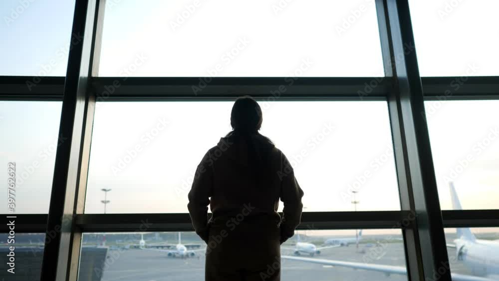 Black silhouette of person looking out of terminal large window at passenger airplanes on air field at contemporary airport backside view Black silhouette of person looking out of terminal large window at passenger airplanes on air field at contemporary airport backside view