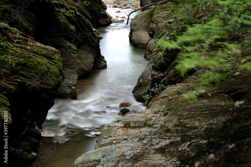 photograph of natural small rapid stream flow from waterfall between rocky cliff canyon taken by slow speed shutter that made some part of the trees blurred © photopk