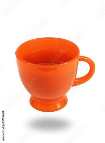 Orange glass teacup full of tea levitating over white surface