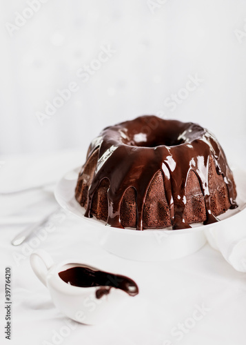 Dark chocolate cake covered with icing on a white stand. Selective focus.