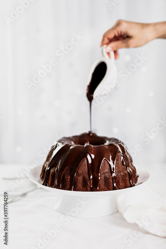 Dark chocolate cake covered with icing on a white stand. Selective focus.