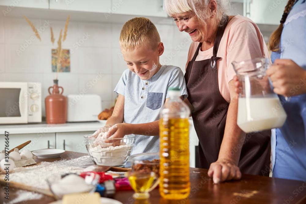 Joyous senior woman happily cooking happily with two grandkids