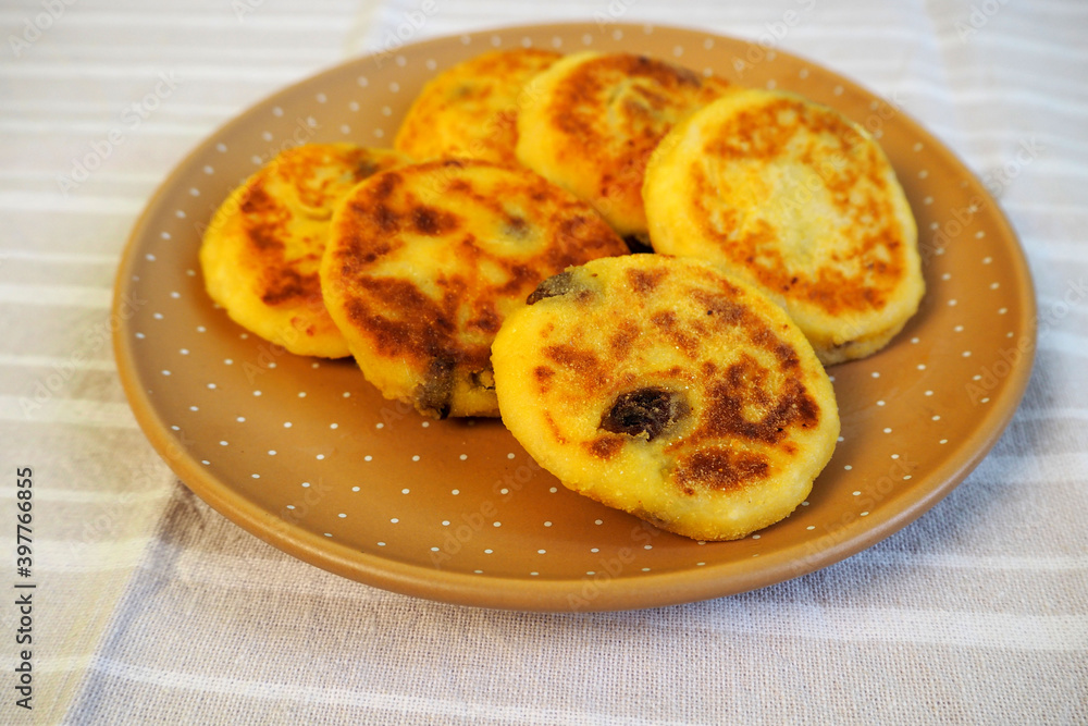 six yellow sugar-free cheesecakes with banana and raisins in corn flour lie in a brown polka-dot round plate on a light white and gray striped tablecloth side view . cooking cheesecakes at home six yellow sugar-free cheesecakes with banana and raisins in corn flour lie in a brown polka-dot round plate on a light white and gray striped tablecloth side view . cooking cheesecakes at home
