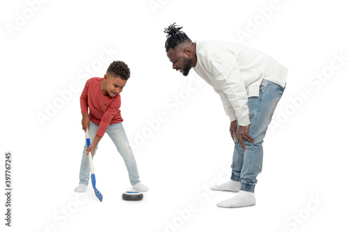 Dark skinned African male and his little son have fun playing hockey together, isolated