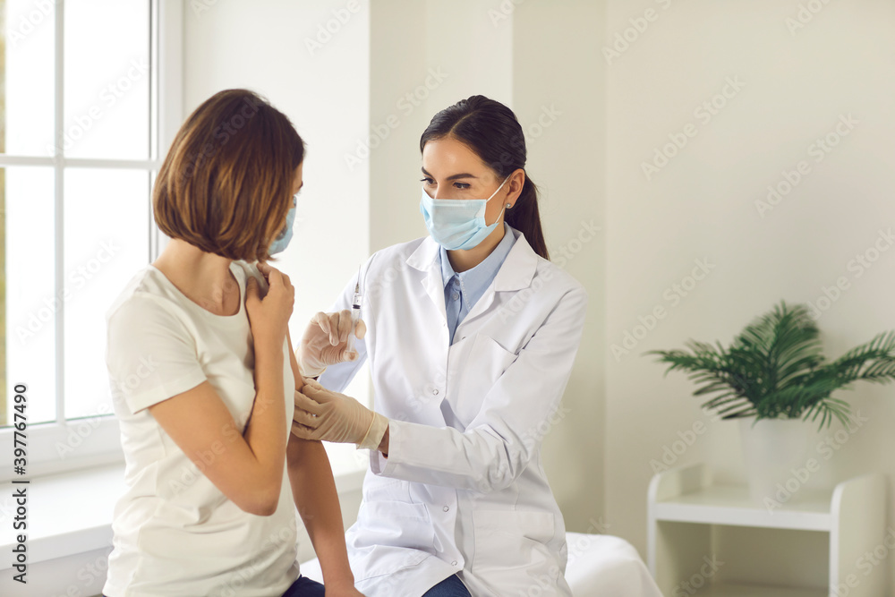 Professional nurse in a medical face mask giving an antiviral vaccine to a young woman