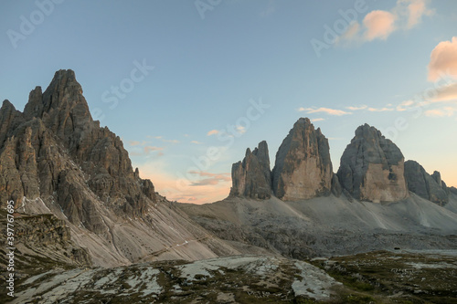 A panoramic capture of the sunset above Tre Cime di Lavaredo (Drei Zinnen) and surrounding mountains in Italian Dolomites. The mountains are surrounded by pink and orange clouds. Golden hour. Serenity photo