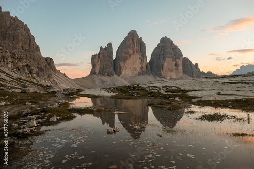 Golden hour over the Tre Cime di Lavaredo (Drei Zinnen), mountains in Italian Dolomites. The peaks reflect in a paddle. The mountains are surrounded with orange and pink clouds. Sunset time. Serenity