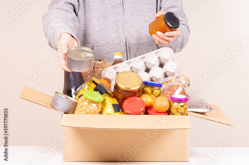 Volunteer hands with food donation box full of grocery products on white desk