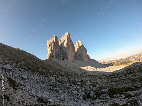 A panoramic view on the first sunbeams reaching the top of the Tre Cime di Lavaredo  Drei Zinnen   Italian Dolomites. The peaks shine with pink and orange. New day beginning in the high mountains