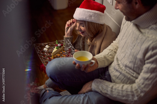 Charming woman in Santa hat and sweater holding tasty cake in hand near handsome man