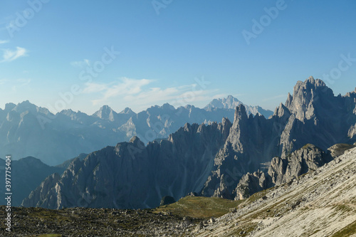 Panoramic view on Italian Dolomites. Endless, high and sharp mountains from each side. The peaks are shrouded in morning haze. Narrow pathway going along the mountain slope. Remote and isolated place