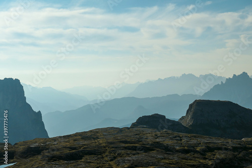 A view on a vast valley in Italian Dolomites. The valley is surrounded with high mountains from each side. Strong, early morning sun. There are a few clouds above. Remote and isolated place. Remedy