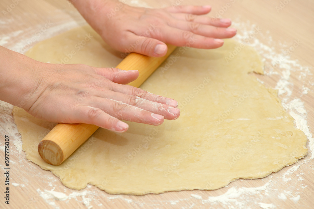 Women's hands roll out the dough with a rolling pin Women's hands roll out the dough with a rolling pin