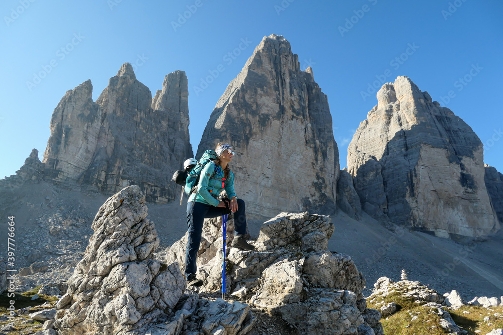 A woman standing on a big boulder and enjoying the close up view on the Tre Cime di Lavaredo (Drei Zinnen), mountains in Italian Dolomites. Sharp and high mountain wall. Desolated and raw landscape